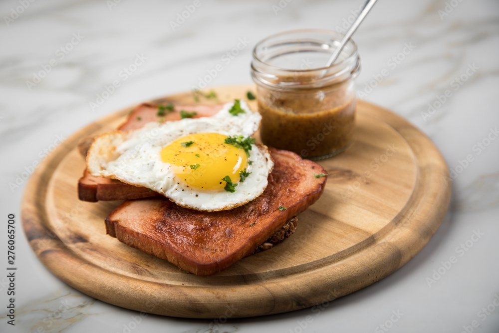 Gebräunter Bayrischer Leberkäse mit gebratenen Spiegelei auf Sonnenblumenkernbrot mit süßen Senf auf Holzbrett