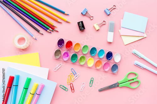 School supplies stationery, colour pencils, paints, paper on pink background, back to school concept with free copy space for text, modern elementary education. Kids desk, flat lay, top view, mockup.