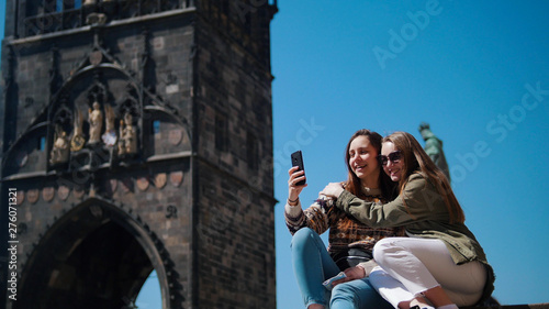 Two young women huging and take a selfie on the background of the historic tower