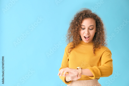 Beautiful African-American woman looking at watch against color background