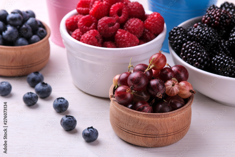 Delicious berries in a bowl, currants, blackberries, blueberries, raspberries on a white wooden table. Delicious berries in a bowl, currants, blackberries, blueberries, raspberries on a white wooden table.
