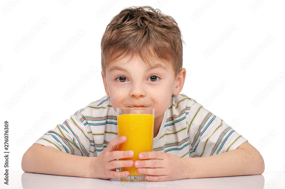 Portrait of happy little boy with glass of orange juice sitting at table on white background. Child is drinking orange juice and looking at camera. Portrait of happy little boy with glass of orange juice sitting at table on white background. Child is drinking orange juice and looking at camera.