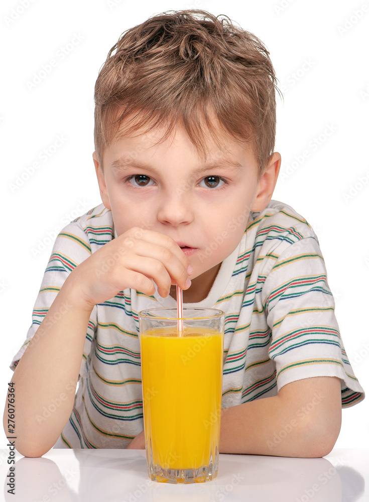 Portrait of happy little boy with glass of orange juice sitting at table on white background. Child is drinking orange juice using straw. Portrait of happy little boy with glass of orange juice sitting at table on white background. Child is drinking orange juice using straw.