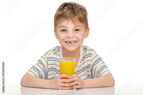 Portrait of happy little boy with glass of orange juice sitting at table on white background.