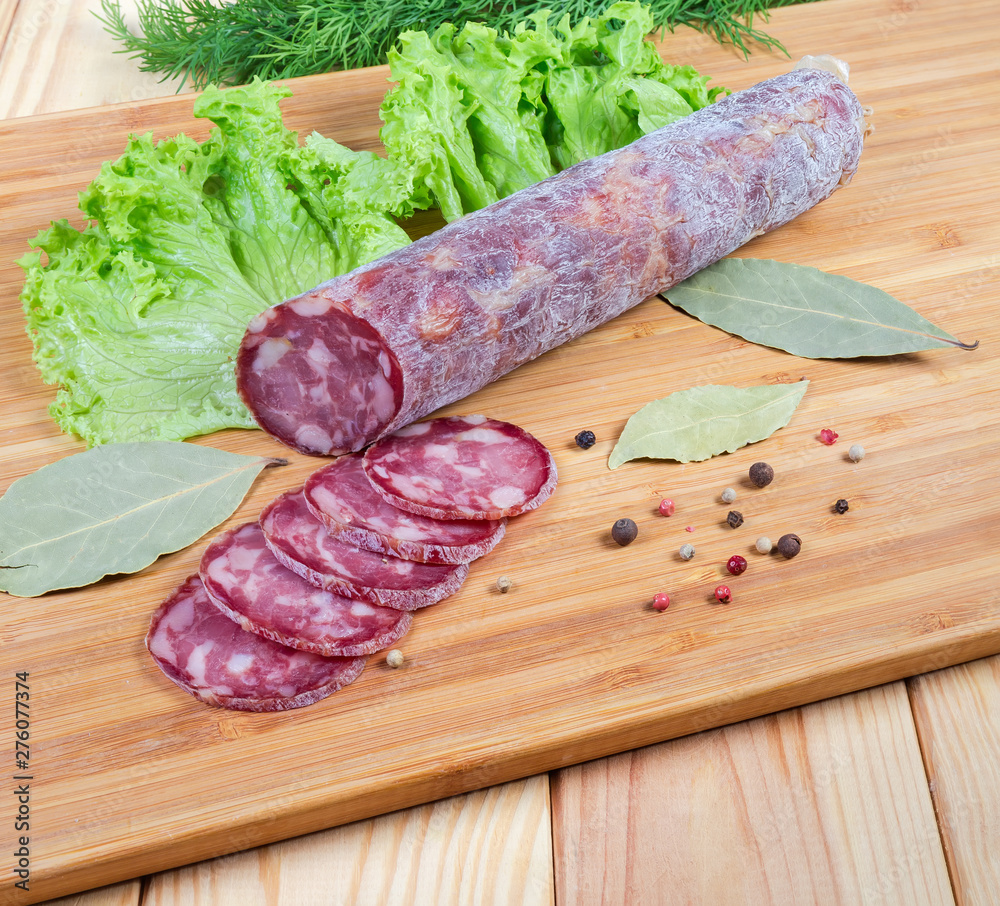 Partly sliced dry-cured sausage, greens, spices on cutting board Partly sliced dry-cured sausage, greens, spices on cutting board