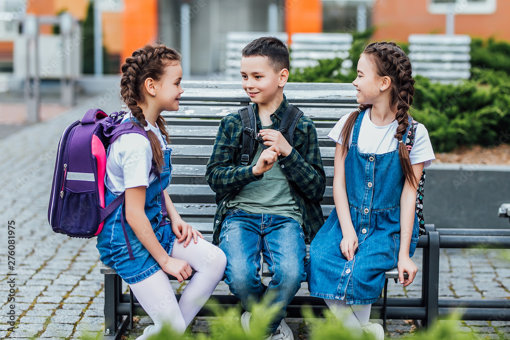 Obraz premium Pupils of primary school. Girls and boy with backpacks near building outdoors. Beginning of lessons. First day of fall.