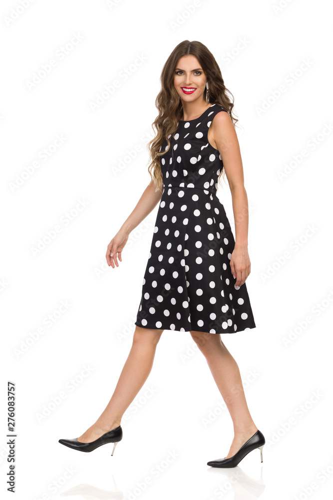 Smiling Beautiful Young Woman In Black Dotted Cocktail Dress And High Heels Is Walking And Lokking At Camera Smiling Beautiful Young Woman In Black Dotted Cocktail Dress And High Heels Is Walking And Lokking At Camera