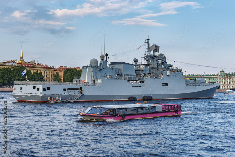 warship and tourist boats on the Neva River against the blue sky and the city