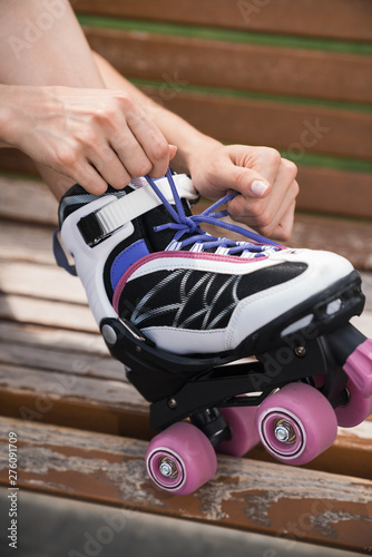 Mid adult woman sitting outdoors on a bench, tying roller skates. close up.