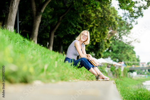 Woman dreaming about vacation. Literature for summer vacation. Girl relaxing at riverside after working day. Rest relax and hobby. Summer vacation. Girl sit on green grass near river and read book