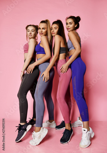 Young tall athletic women in blue, grey, brown standing behind each other. Fitness girls posing on pink background. 