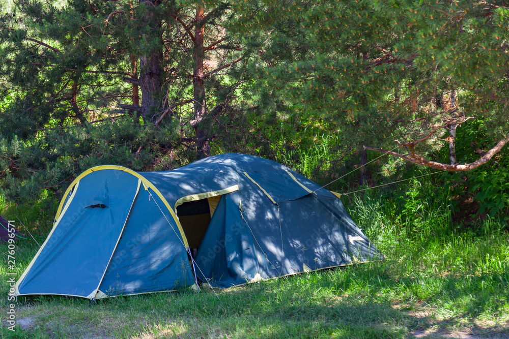 Tent camping in the shade of coniferous green trees on a sunny summer day. Extreme sports and outdoor recreation without people in the wilderness. Tent camping in the shade of coniferous green trees on a sunny summer day. Extreme sports and outdoor recreation without people in the wilderness.