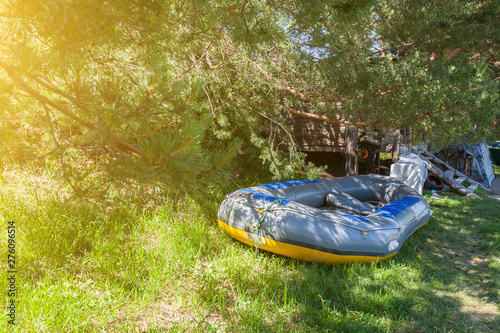 Tent camping in the shade under the trees with a wooden house and a large inflatable rafting boat near the river in the Altai Mountains. Extreme sports and recreation.