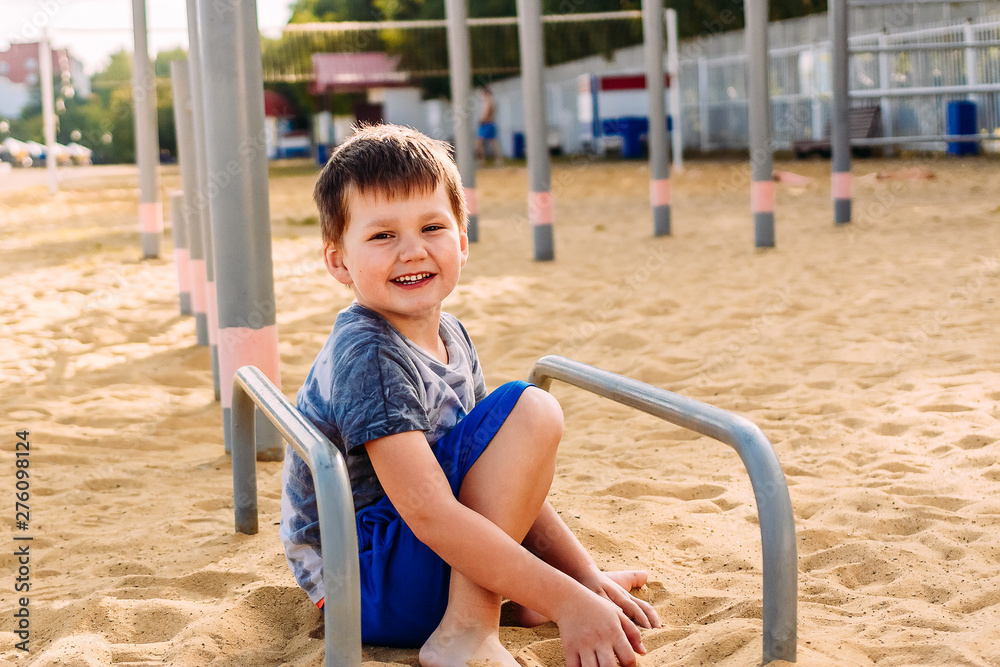 smiling five-year-old boy sitting on the yellow sand on the beach smiling five-year-old boy sitting on the yellow sand on the beach