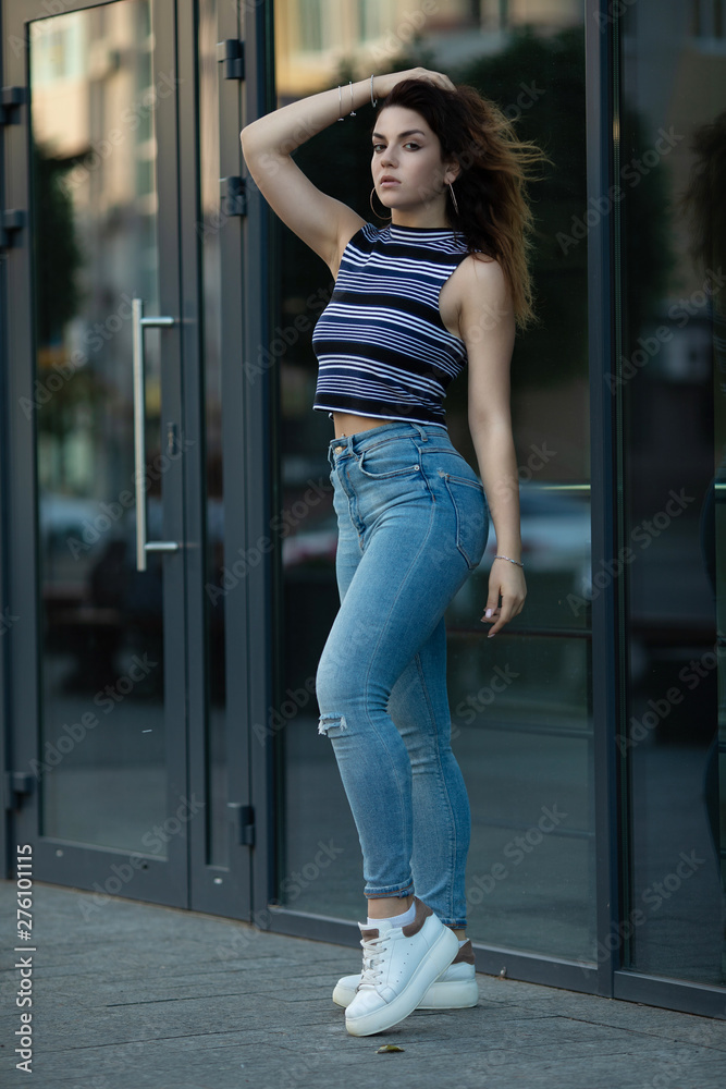 Beautiful girl in T-shirt, high waist jeans and white shoes standing outdoor.