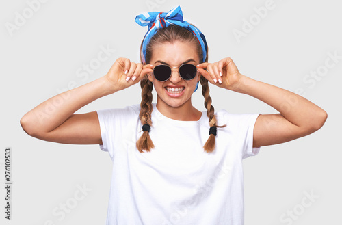 Attractive blonde young woman wearing trendy sunglasses, white t-shirt and blue headband, smiling broadly. Student girl going crazy with braids hairstyle. People and emotions