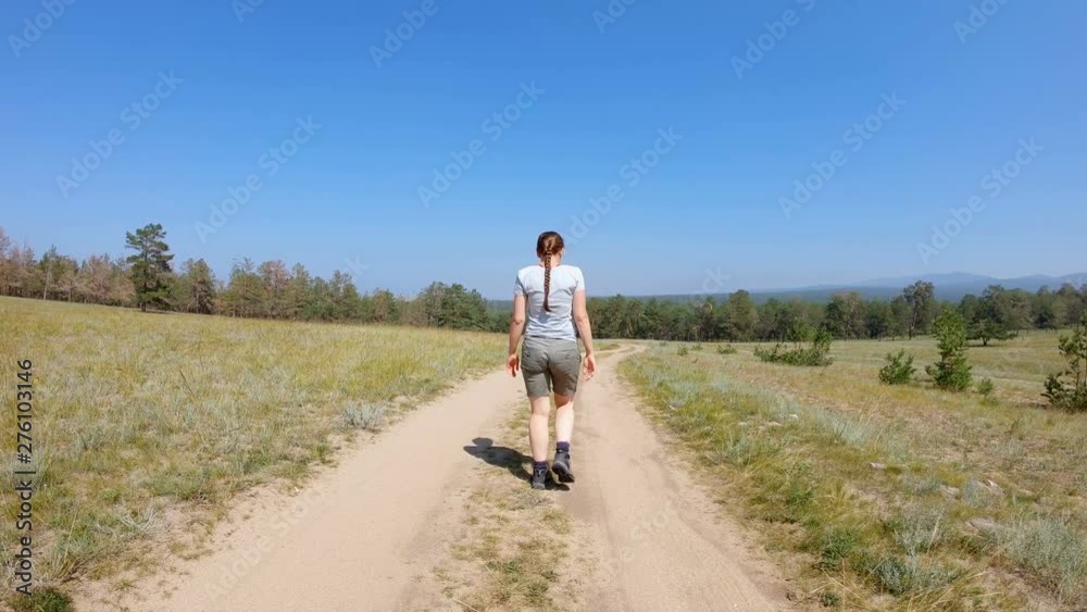 Young girl with braid in shorts and t-shirt walking on a country road. Back view, gimbal shot, slow motion Young girl with braid in shorts and t-shirt walking on a country road. Back view, gimbal shot, slow motion