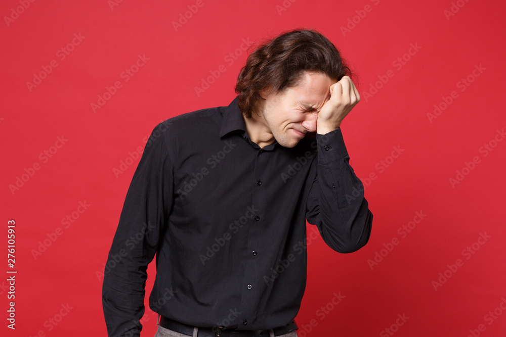 Young sad curly long haired man in black shirt standing posing isolated on red wall background studio portrait. People sincere emotions lifestyle concept. Mock up copy space. Problem crisis depression Young sad curly long haired man in black shirt standing posing isolated on red wall background studio portrait. People sincere emotions lifestyle concept. Mock up copy space. Problem crisis depression