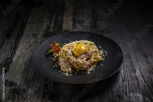 Super tasty bolognese carbonara pasta on a black plates onto dark wooden table. Menu for restaurant