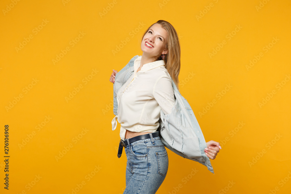 Obraz premium Portrait of cheerful smiling pretty young woman in denim casual clothes standing, looking up isolated on bright yellow orange wall background in studio. People lifestyle concept. Mock up copy space.
