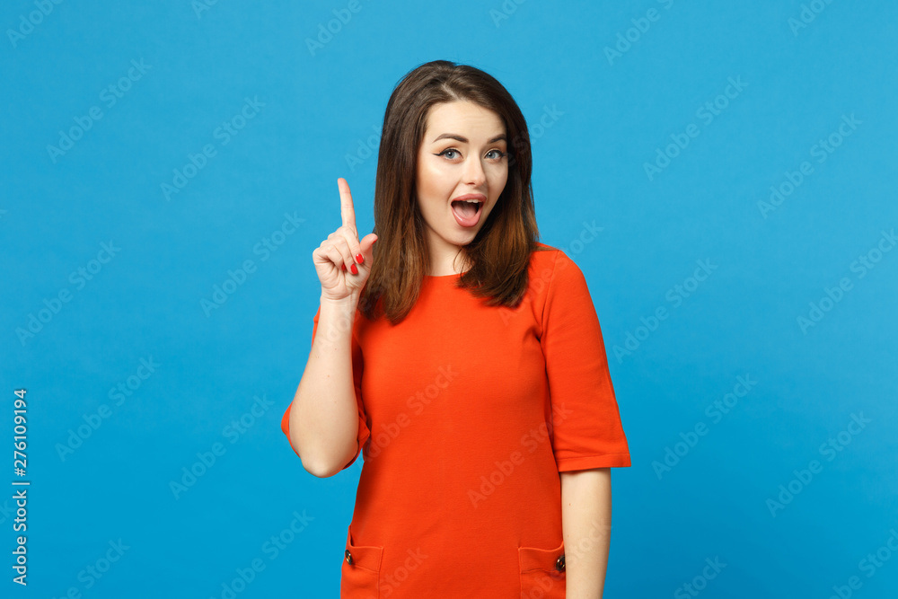 Beautiful young woman wearing red orange dress holding index finger up with great new idea isolated over trendy blue background, studio portrait. People lifestyle fashion concept. Mock up copy space. Beautiful young woman wearing red orange dress holding index finger up with great new idea isolated over trendy blue background, studio portrait. People lifestyle fashion concept. Mock up copy space.