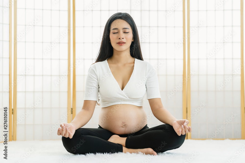 Fototapeta premium Asian Pregnant doing exercises with yoga by sitting and Meditating in japanese style house on the whit carpet, pregnant exercise concept, preparing to be motherhood with good healthy