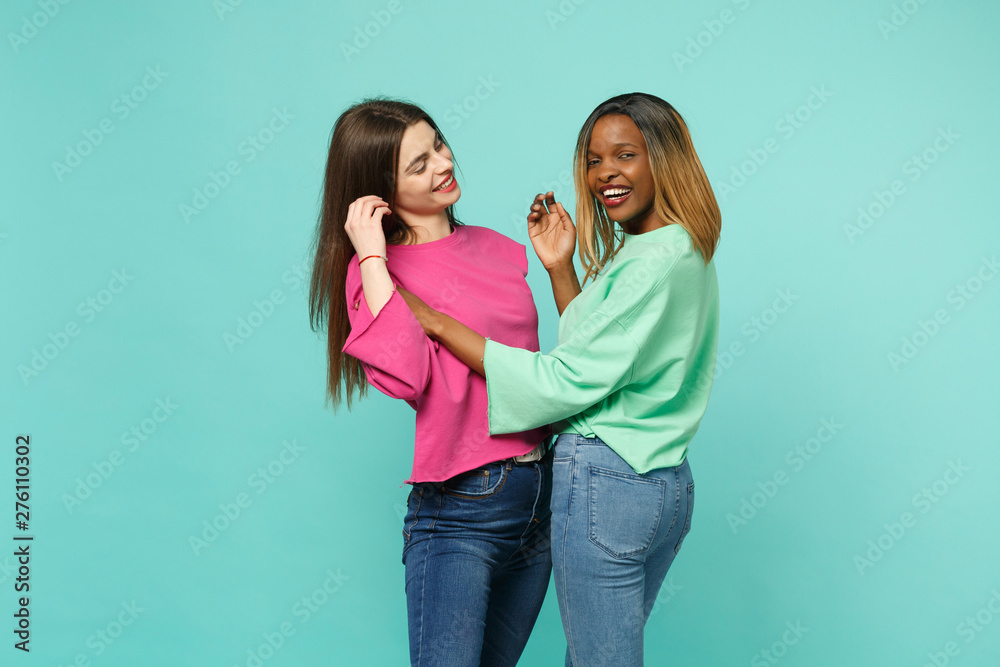 Two young women friends european and african american in pink green clothes dancing fooling isolated on blue turquoise wall background, studio portrait. People lifestyle concept. Mock up copy space. Two young women friends european and african american in pink green clothes dancing fooling isolated on blue turquoise wall background, studio portrait. People lifestyle concept. Mock up copy space.