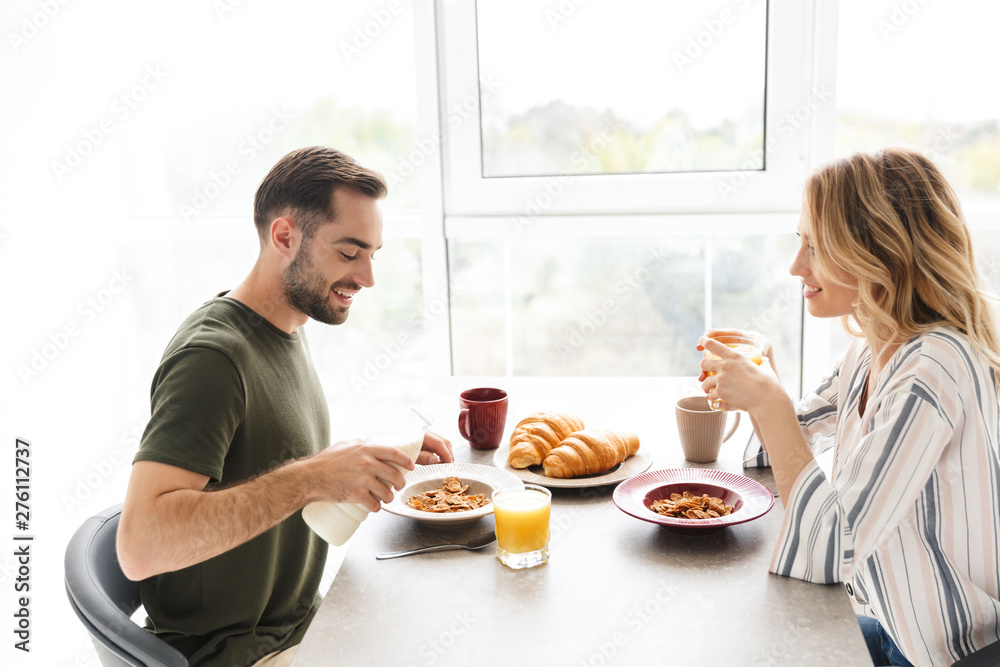 Happy young loving couple indoors at the kitchen have a breakfast eat croissant and corn flakes with milk. Happy young loving couple indoors at the kitchen have a breakfast eat croissant and corn flakes with milk.