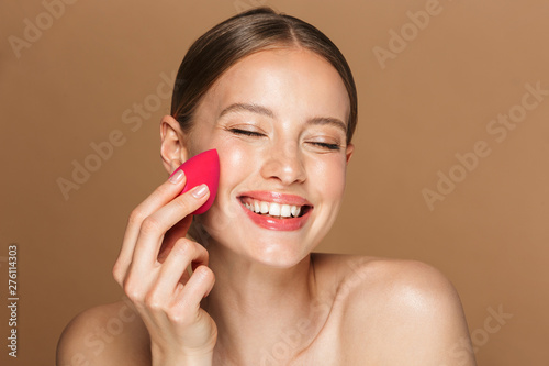 Принти на полотні Cheerful happy young amazing woman posing isolated over brown chocolate background wall holding makeup sponge