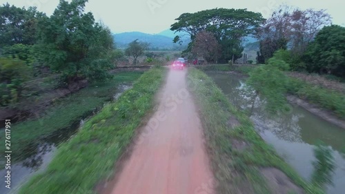 A straight wide shot of grasses growing along an untarred road and water flowing by both sides of the road photo