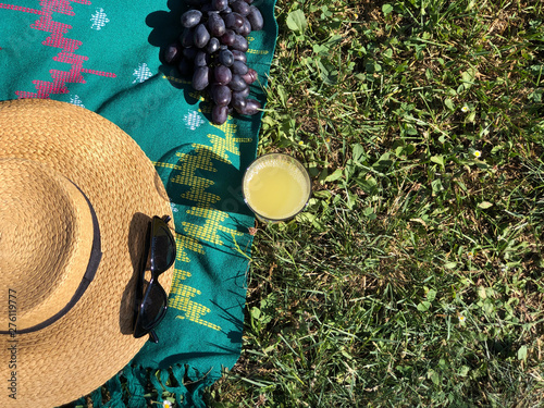 Straw hat, blanket, sunglasses, grapes and glass juice on green grass background. Summer concept. Copy space. Picnic blanket 
