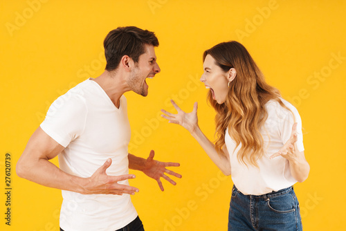 Photo of furious aggressive couple man and woman in basic t-shirts screaming at each other while standing face to face photo