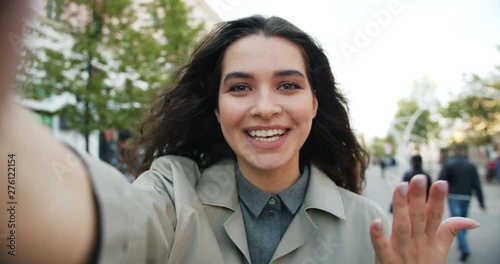 POV slowmotion of attractive woman making online video call in the street talking gesturing looking at camera outdoors. Communication and youth concept. photo