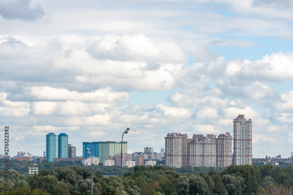 Fototapeta premium View of the new residential area of Moscow among the green grove on the background of clouds in the blue sky.