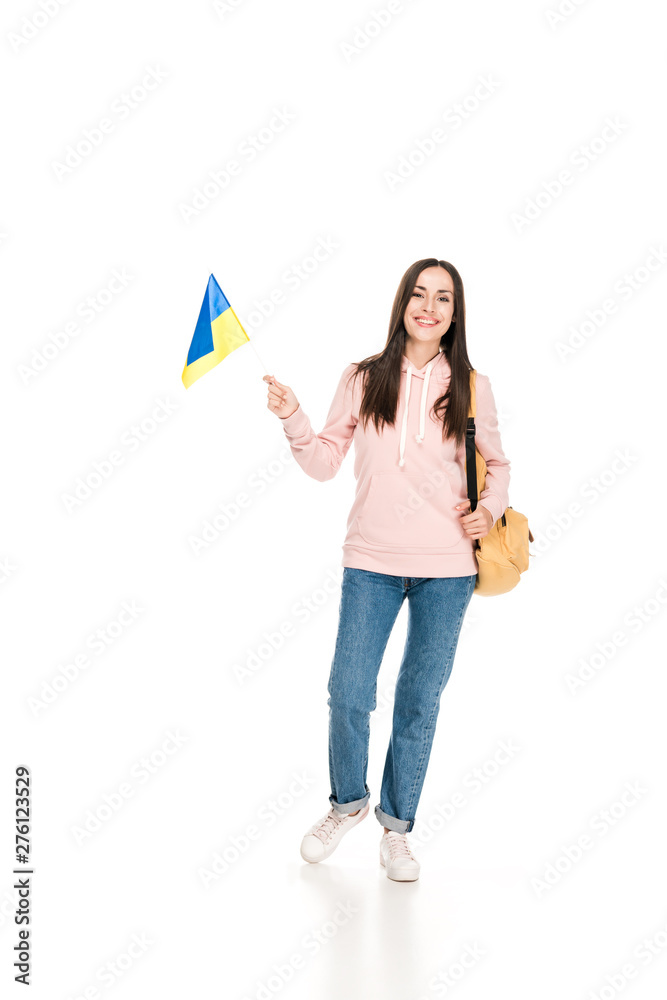full length view of smiling brunette girl with backpack holding Ukrainian flag isolated on white full length view of smiling brunette girl with backpack holding Ukrainian flag isolated on white