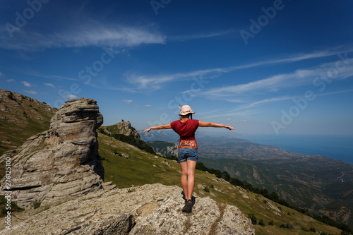 The concept of overcoming, rest and freedom. A woman with tanned legs is standing on top with her arms wide open on either side. Near the rocks of unusual shape. 