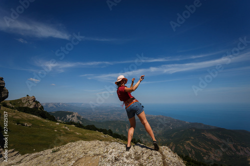 Happy woman in short shorts and wearing a hat is dancing on the top of a mountain. The concept of freedom, recreation, travel. Good luck and success. When dreams come true.
