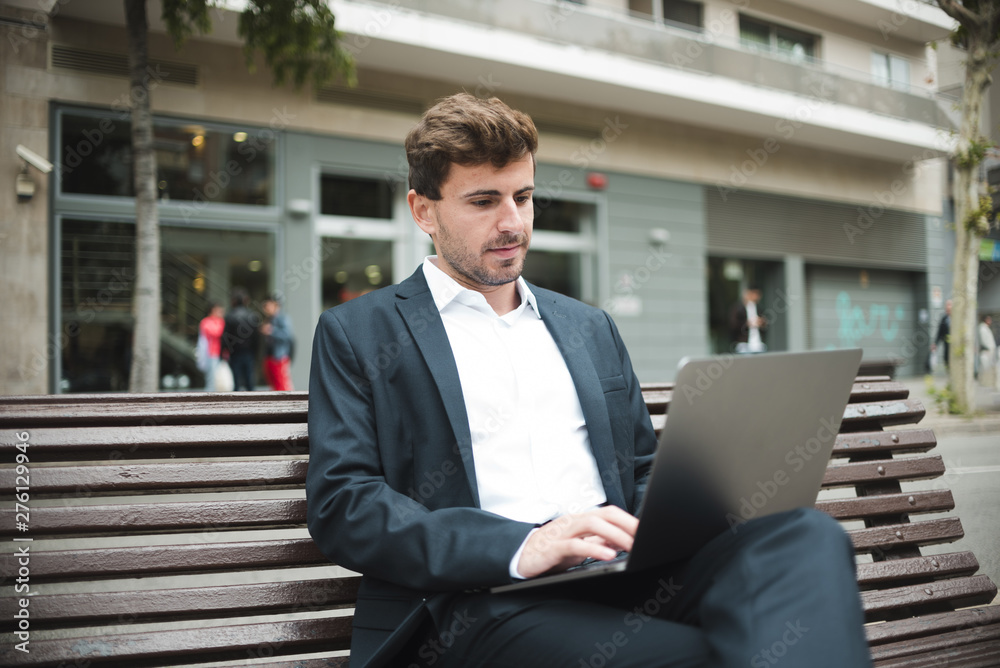Portrait of a young businessman sitting on bench using laptop Portrait of a young businessman sitting on bench using laptop