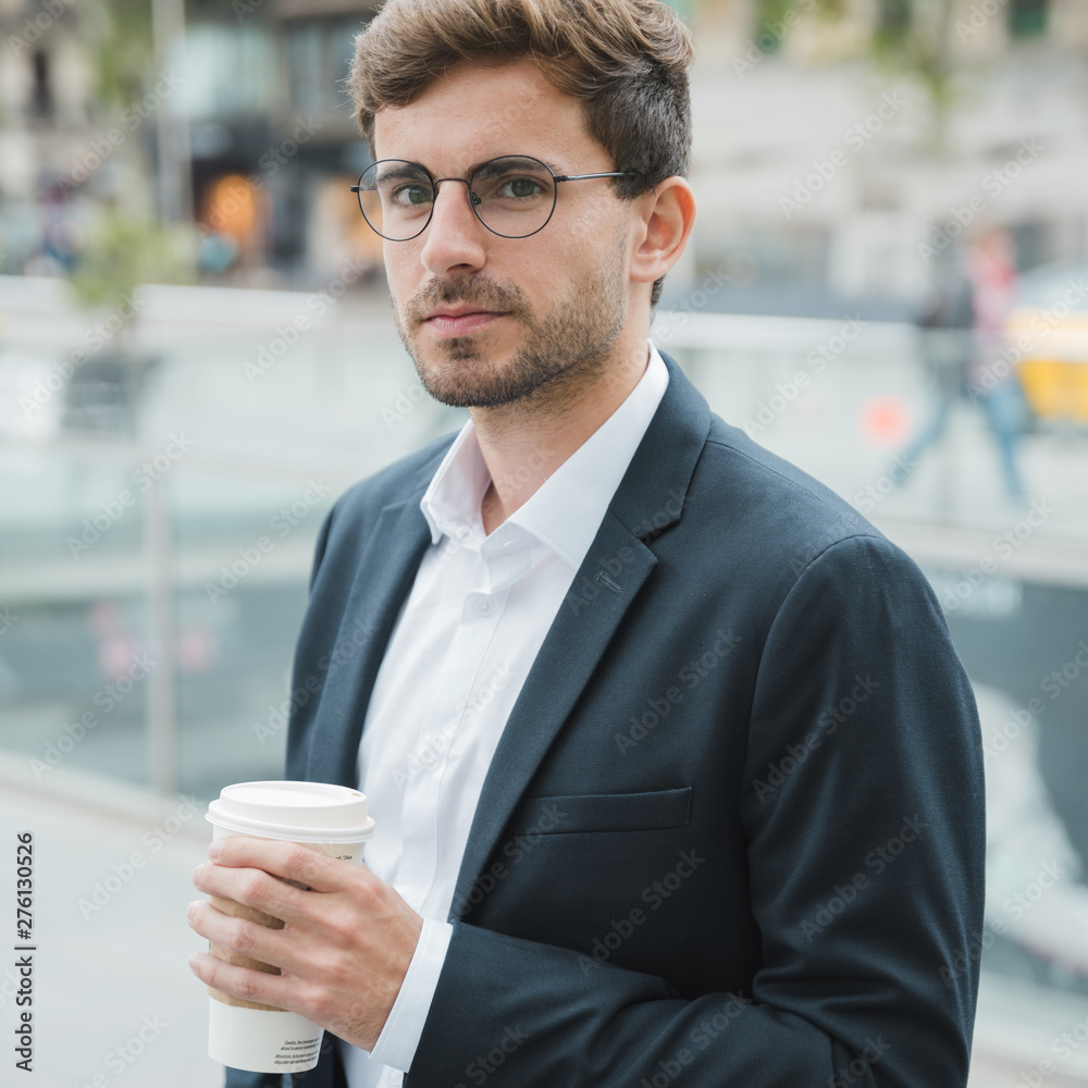 Close-up of a young businessman holding disposable coffee cup in hand looking at camera Close-up of a young businessman holding disposable coffee cup in hand looking at camera