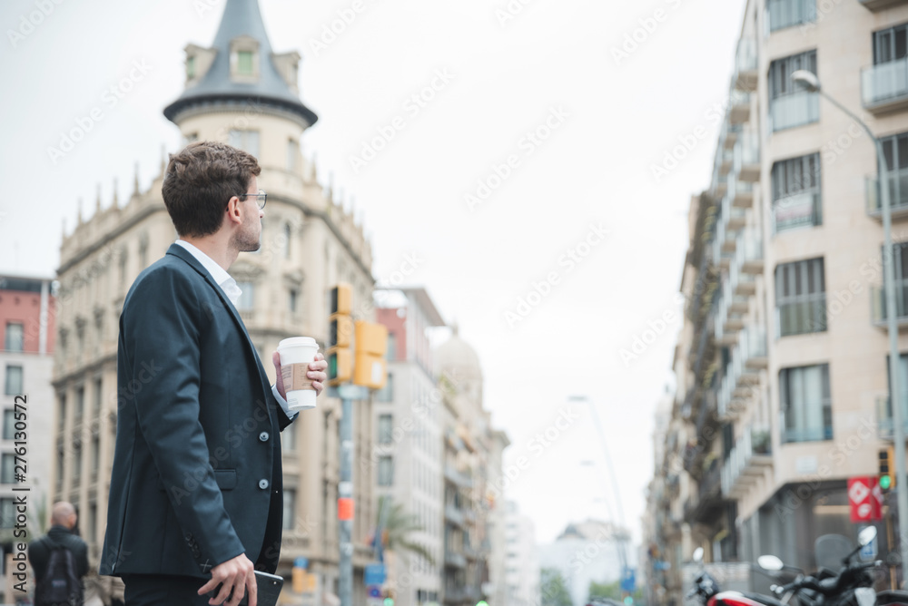 Young businessman holding coffee cup in hand looking at buildings in the city
