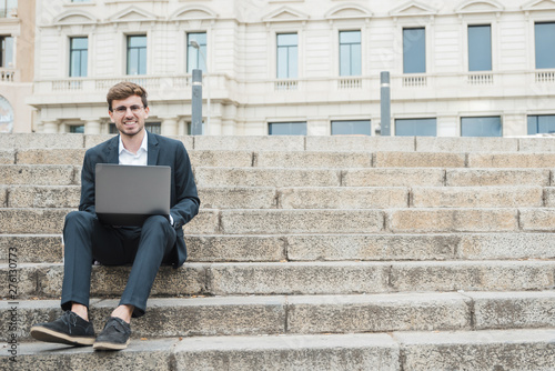 Smiling portrait of a young businessman sitting on staircase using digital tablet