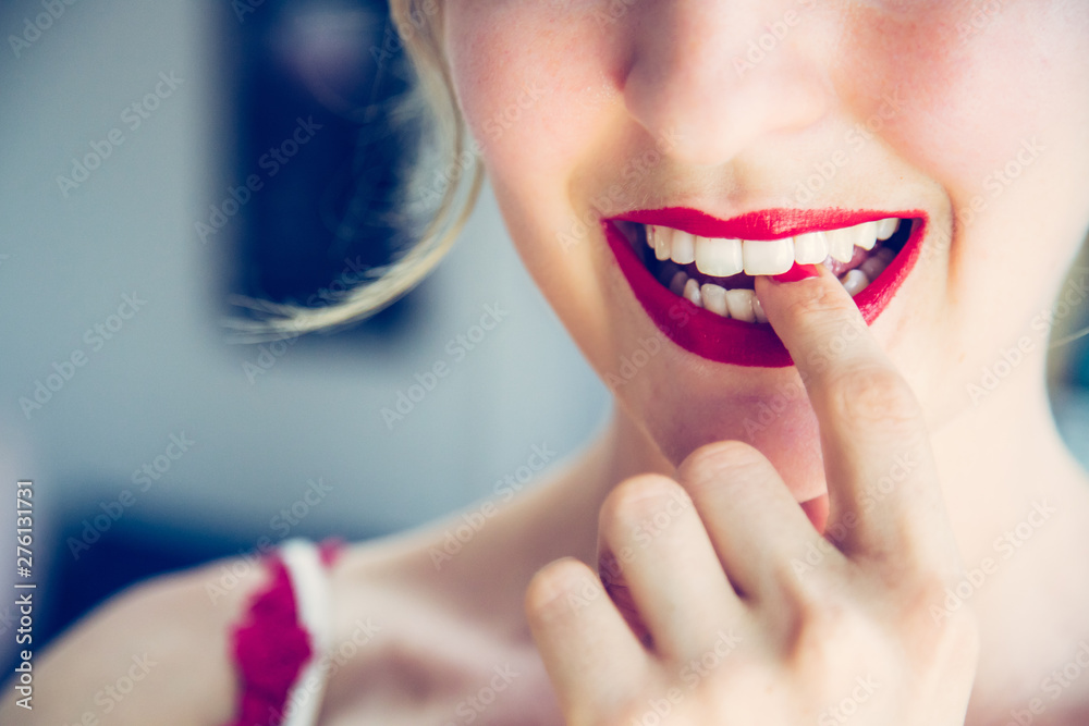 Attractive red lip stick: Blonde young woman with colorful nail polish is looking herself in the mirror. Cut out of the face. - obrazy, fototapety, plakaty 