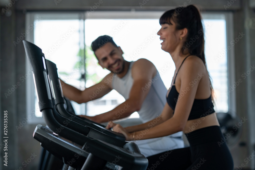 Defocused blurred medium shot of active man and woman smiling while doing aerobic cardio workout on training exercise bike at the fitness gym. Healthy weight loss fit and firm concept.