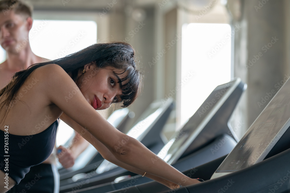 Selective focus tired young beautiful woman in fitness sportswear taking a break from running jogging workout cardio on treadmill machine at the fitness gym. Healthy weight loss fit and firm concept. Selective focus tired young beautiful woman in fitness sportswear taking a break from running jogging workout cardio on treadmill machine at the fitness gym. Healthy weight loss fit and firm concept.