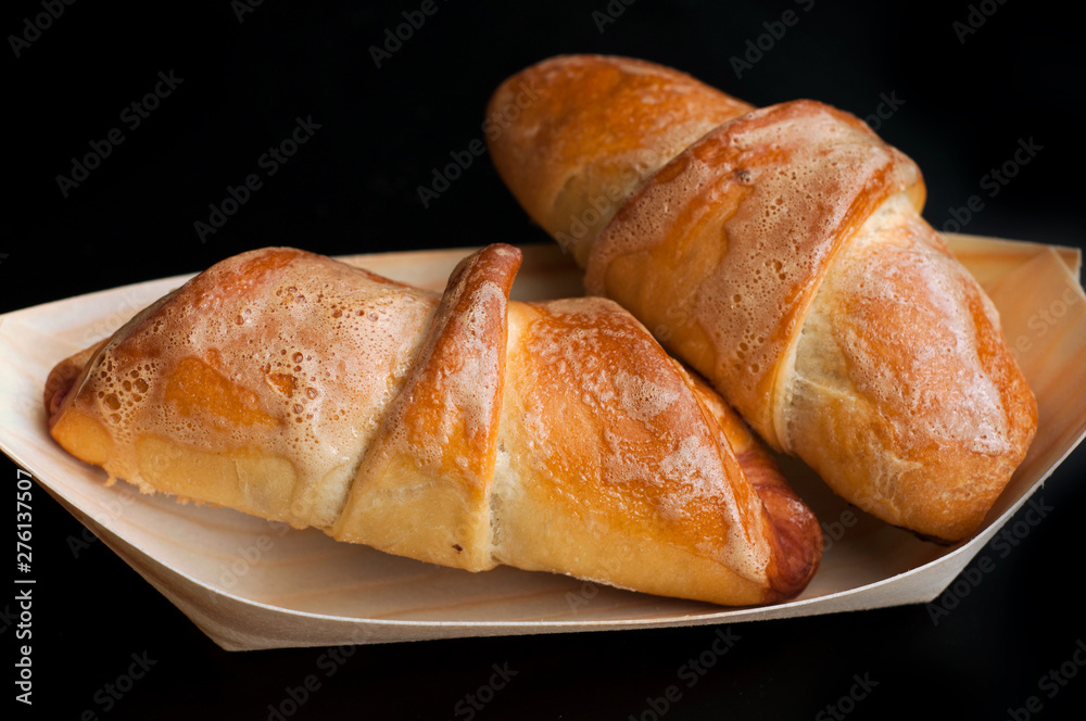 Homemade croissants in a bio wooden dish, isolated on black background