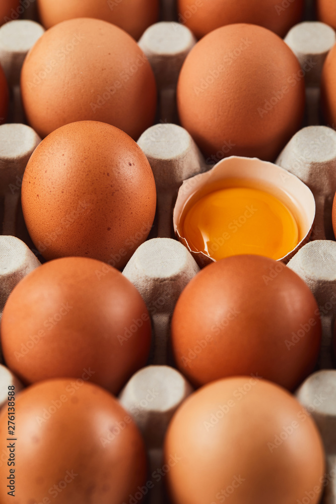 selective focus of broken eggshell with yellow yolk near eggs in carton box selective focus of broken eggshell with yellow yolk near eggs in carton box