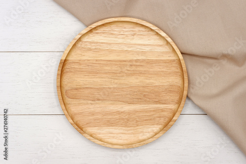 Empty round wooden plate with beige tablecloth on white wooden table. Top view image.
