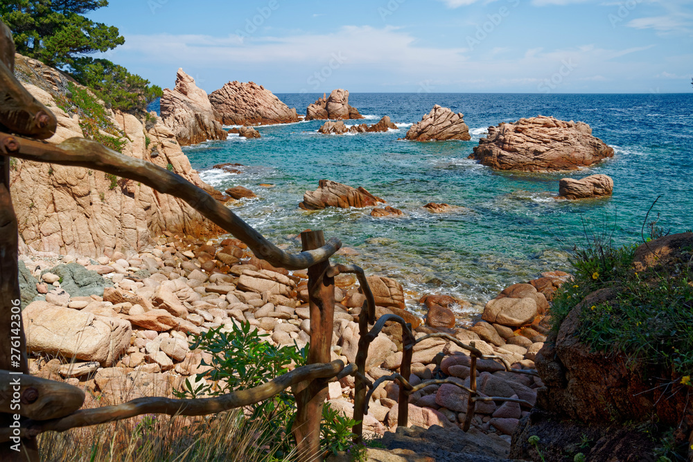 Rugged rock formation with wooden staircase at a turquoise beach at La Sorgente, Costa Paradiso in Sardinia (Italy) with turquoise blue sea
