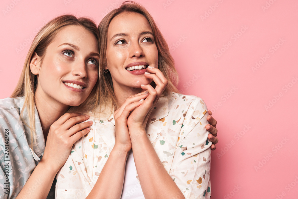 Smiling pleased beautiful blondes women friends posing isolated over pink wall background looking aside. Smiling pleased beautiful blondes women friends posing isolated over pink wall background looking aside.