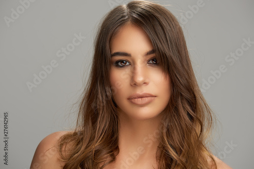 Headshot of beautiful Caucasian brunette posing in front of grey background. Beauty photography.